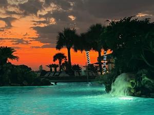 una piscina con cascada y palmeras al atardecer en Ocean front condo, en Panama City Beach