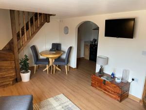 uma sala de estar com uma mesa e cadeiras e uma televisão em Buttercup Cottage at The Old Tractor Barn em Brackley