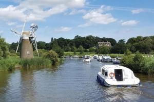 a boat in the water next to a windmill at Bespoke Chalet 214, walk to the beach & close to Norfolk broads - pet friendly! in Great Yarmouth