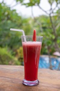 a red drink with a piece of fruit in a glass at Arunika Cottage in Nusa Penida