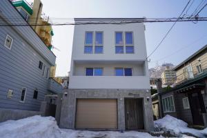 a white house with a garage in the snow at Hakodate MOTOMACHI guesthouse in Hakodate