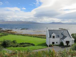a white house on the shore of a body of water at Macinnisfree Cottage in Saasaig