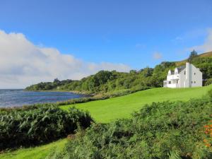 a white house on a hill next to the water at Macinnisfree Cottage in Saasaig