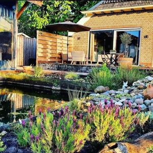 einen Garten mit einem Teich und eine Terrasse mit einem Sonnenschirm in der Unterkunft The Barn - Aurora Hoeve - loft met jacuzzi in Oldekerk
