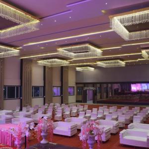 une salle de banquet avec des tables blanches, des chaises et des lustres dans l'établissement Hotel Emperor Paradise, à Bilāspur