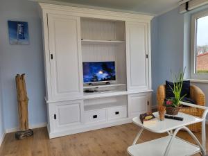 - un salon avec une télévision dans un meuble blanc dans l'établissement Ferienhaus Annas Garten, à Sankt Peter-Ording