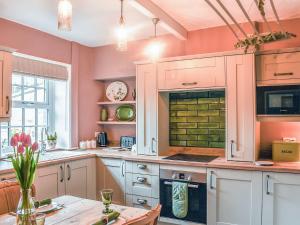 a kitchen with pink walls and white cabinets and a table at Honey Cottage in Gargrave