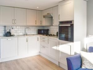 a white kitchen with white cabinets and a blue chair at Willow Tree Farm in Sutton on Sea