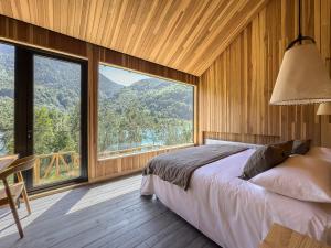 a bedroom with a bed and large windows at Tawa Refugio del Puelo in Puelo