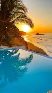 a pool with a palm tree and a sunset at LAOLA SURF CAMP EL SUNZAL in La Libertad