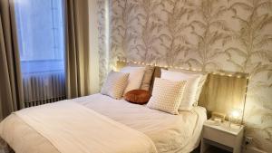 Cette chambre comprend un lit avec des draps blancs et du papier peint. dans l'établissement Appartement Cosy - En face de la gare, au centre ville, à Épinal