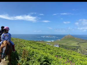 a girl riding a horse on a hill overlooking the ocean at Syds Corner bell tent in St. Just