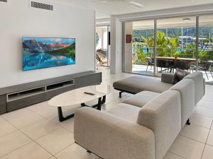 een woonkamer met een bank en een tv aan de muur bij Blue on Blue Apartment 317 in Nelly Bay