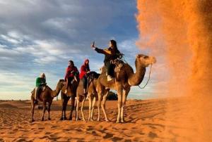 a group of people riding on camels in the desert at Désert Man luxury Camp in Merzouga
