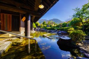 una piscina de agua junto a un edificio con montañas en el fondo en Ryosou Makibanoie 18 years or older, en Yufu