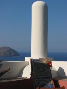 una sedia seduta di fronte a un edificio bianco con l'oceano di Casa Rossa del Cappero Sottano a Città di Lipari