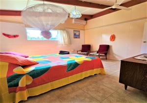 1 dormitorio con 1 cama colorida con 2 sillas y ventana en Ann's Beach House, en Rarotonga