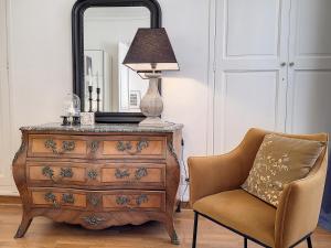 a dresser with a lamp and a chair next to a mirror at Escale citadine au centre d'Avignon, climatisation, appartement de charme, spacieux et lumineux in Avignon