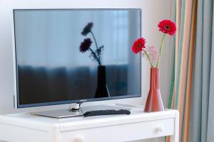 a tv on a white cabinet with two vases and flowers at Top Appartements Roth am Strande in Westerland (Sylt)