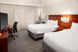 a hotel room with two beds and a desk and a television at Courtyard by Marriott Houston Rice University in Houston