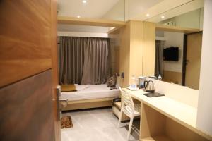 a small room with a bed and a desk with a kitchen at Maple Inn in Thane