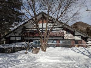 a house in the snow with a tree in front of it at Tanigawa Valley Lodge & Coffee Roastery in Minakami