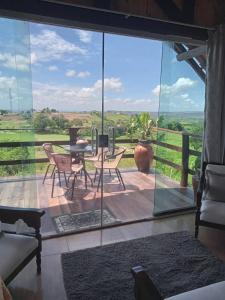 eine Terrasse mit einem Tisch und Stühlen sowie einem großen Glasfenster in der Unterkunft Chalé Mirante da Pedra in Serra de São Bento