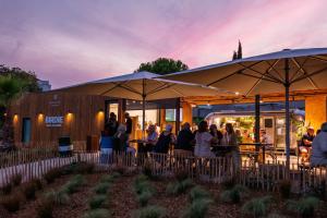 un grupo de personas de pie fuera de un restaurante con sombrillas en Résidence Les Jardins de Massane en Baillargues