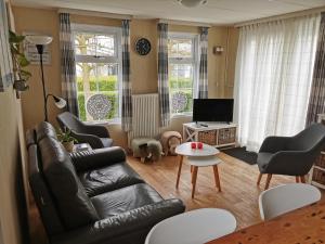 uma sala de estar com um sofá de couro preto e cadeiras em Chalet - Dà gae nog à em Baarland