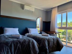 a bedroom with two beds and a large window at Apartamentos Rossa Residenzialle CENTRO by Achei Gramado in Canela