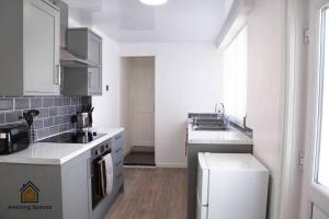 a white kitchen with a sink and a stove at Spacious 3 bed Terrace House with free parking & free Wi-Fi by Amazing Spaces Relocations Ltd in Saint Helens