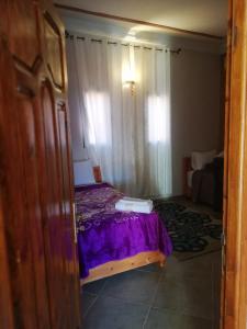 Un dormitorio con una cama con sábanas moradas y una ventana en Riad Ouinz en Aït Ben Haddou