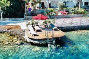 a wooden deck with chairs and an umbrella in the water at Bodrum’da Özel İskeleli 4+1 Yalı Dairesi in Bodrum City