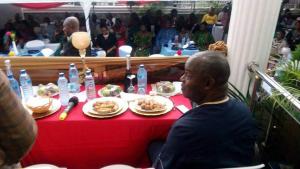 mężczyzna siedzący przy czerwonym stole z talerzami jedzenia w obiekcie Blue-View Suites & Apartments w mieście Abudża