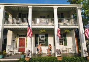 Duas mulheres sentadas no alpendre de uma casa branca com bandeiras americanas. em Blue Ruby at Grice-Fearing B&B em Elizabeth City