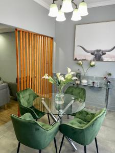 uma sala de jantar com uma mesa de vidro e cadeiras verdes em Mdumela Stays 2 Bedroom Modern City Apartment em Pietermaritzburg