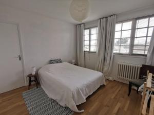 ein weißes Schlafzimmer mit einem Bett und einem Stuhl in der Unterkunft Les Embruns in Bréhal