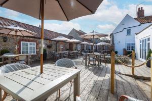 a patio with tables and chairs and umbrellas at The Manor Coastal Hotel & Inn, Blakeney - part of The Coaching Inn Group in Blakeney