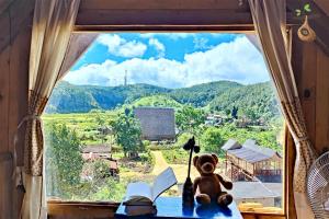 ein Teddybär, der auf einem Tisch sitzt und aus dem Fenster schaut in der Unterkunft Tổ Chim Ri Homestay Măng Đen in Kon Von Kla