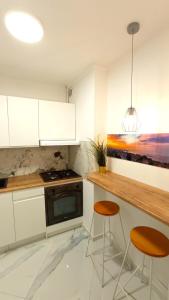 a kitchen with white cabinets and a counter and two stools at Meva Sopot Apartment in Sopot