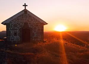 an old stone church with the sunset in the background at Villa Tauria- Casa de campo em aldeia medieval in Sabugal
