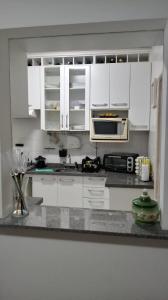 a white kitchen with white cabinets and a microwave at Mar, Praia, Sossego e Tranquilidade in Itanhaém