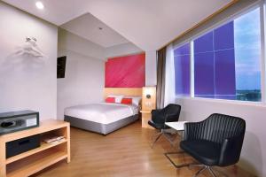 a bedroom with a bed and two chairs and a window at favehotel Jababeka Cikarang in Cikarang