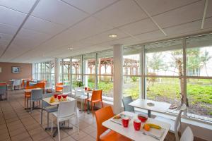 a dining room with tables and chairs and windows at All Suites Appart Hôtel - Bordeaux - Mérignac Aéroport in Mérignac