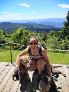 una mujer arrodillada en una terraza de madera con un perro en Idyllisch gelegene Ferienwohnung im Herzen des bayerischen Waldes, en Zachenberg