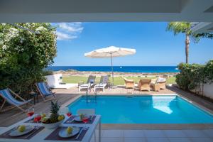 a swimming pool with chairs and an umbrella and the ocean at Jasmine Sea Front Villa in Protaras