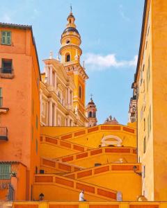 a yellow building with a clock tower and stairs at H&ocirc;tel De Londres in Menton