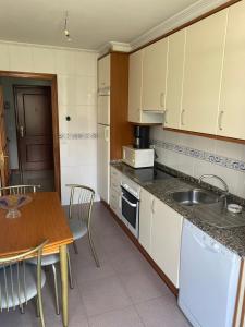 eine Küche mit weißen Schränken, einem Tisch und einem Waschbecken in der Unterkunft APARTAMENTO LADEIRA PLAYA in Baiona
