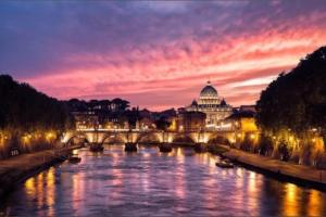 a bridge over a river with a city at night at Casa Benso - near Vatican City and Navona Square in Rome