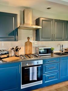 La cuisine est équipée de placards bleus et d'un four avec plaques de cuisson. dans l'établissement Prince Arthur Apartment, à Walton on the Hill